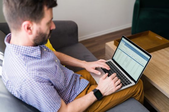 Young man sitting on the sofa and typing on his laptop with a blank screen and copy space